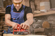 © Виталий Сова - Portrait of a  young man  carpenter using electric sanding machine to polish a wood barin workshop