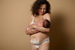 © Taras Grebinets - Authentic mom in underwear, smiles looking at her newborn baby she's holding, shows her body with postpartum scars flaws