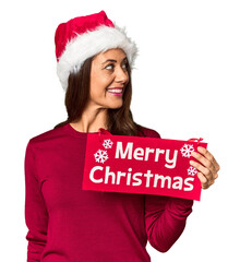 Wall Mural - Middle-aged woman with Merry Christmas sign in studio looks aside smiling, cheerful and pleasant.