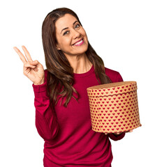 Wall Mural - Middle-aged woman with Valentine's Day heart box in studio joyful and carefree showing a peace symbol with fingers.