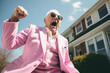 Excited grandfather man wearing glasses and pink pastel color suit celebrating success. Happy overjoyed businessman walking outside and showing yes gesture and laughing.