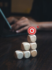 Poster - 3d Target goal icon on wooden sticks bar graph chart steps on desk while businessman working with laptop, vertical style. Business market growth, effort, profit, investment, financial trend concepts.