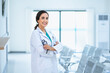 © bigy9950 - Attractive smiling female doctor wearing a white medical gown and holding a stethoscope, standing in the hospital corridor. Medicine and health care concept with copy space. looking at camera.