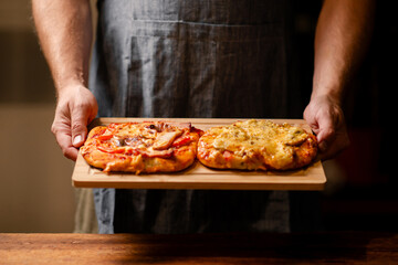 Wall Mural - Rustic Pizza Moment: A snapshot of male hands showcasing two small homemade pizzas on a wooden board