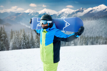 Wall Mural - Portrait Of Man On The Background Of Mountains And Blue Sky, Holding Snowboard And Wearing Ski Glasses. Ski Goggles Of Snowboarder With The Reflection Of Snowed Mountains. Winter Sports