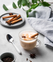 Wall Mural - Traditional Indian masala chai latte in a glass cup. Hot drink with milk, spices and herbs on a light background