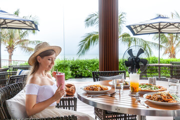 Wall Mural - Serene oceanfront dining setting, woman with sunhat enjoys diverse dishes, ultimate holiday indulgence.