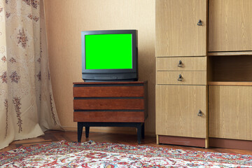 Antique TV with green screen on an antique wooden cabinet, old design in a house in the style of the 1980s and 1990s.