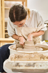 Wall Mural - Artisan woman shaping clay on pottery wheel while working in her workshop. Hobby and handicraft concept.