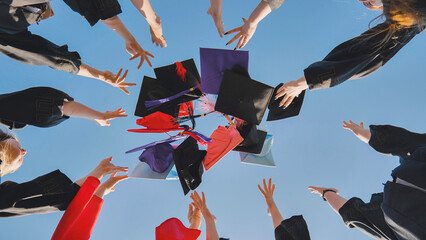 Wall Mural - Graduates tossing multicolored hats against a blue sky.