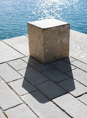 Concrete cube or cement brick with shadow. Abstract photo. Stone cube close-up with blue sea on the background