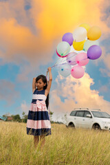 Wall Mural - Cheerful cute girl holding balloons running on green meadow white cloud and blue sky with happiness. Hands holding vibrant air balloons play on birthday party happy times summer on sunlight outdoor