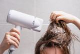Young woman drying her hair with hairdryer in the bathroom close-up front view.