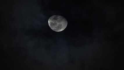 Wall Mural - Bright white moon craters and ridges rises in sky as clouds pass below at night