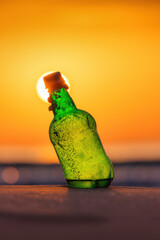 Wall Mural - Bottle on the beach sand and water during golden sunrise over the sea horizon