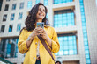 © Dragana Gordic - Beautiful happy young woman messaging on smartphone on the background of a city street on a sunny day. Business woman is looking away and smiling.