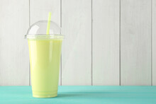 Tasty Smoothie In Plastic Cup On Light Blue Table Against White Wooden Wall. Space For Text