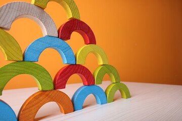 Canvas Print - Colorful wooden pieces of educational toy on light table against orange wall, closeup and space for text. Motor skills development