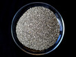 Chia seeds in a glass saucer on a black background, top view