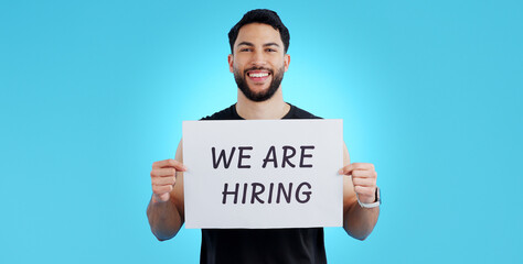 Canvas Print - Portrait, smile and man with we are hiring, poster or announcement in studio on blue background. Recruitment, banner and face of male model with news, announcement or business, opportunity or offer