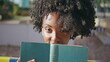 © stockbusters - Portrait african american student posing holding book near face at sunny street.