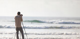 Fototapeta Natura - Young handsome photographer with a tripod and a camera on the beach
