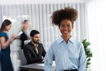 Young African businesswoman portrait poses confidently with diverse coworkers in busy meeting room in motion blurred background. Multicultural team works together for business success. Concord