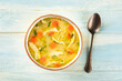 Chicken noodle soup with vegetables, a bowl of healthy stock with a spoon, top shot on a rustic wooden table, winter comfort food