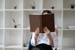 A picture of a woman sitting and reading with a book covering her face.