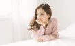 Beautiful Asian woman smiling friendly relax in bedroom. Smiling Korean or Japanese girl hand on chin adorable wearing pink sweater in winter season. Cozy domestic atmosphere on beautiful winter time