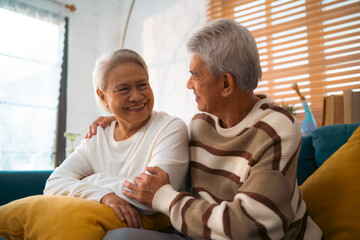 Wall Mural - Sweet older couple enjoys quiet time together, seated comfortably on their vintage couch in a warm, inviting living room, reminiscent of decades of love and shared moments.