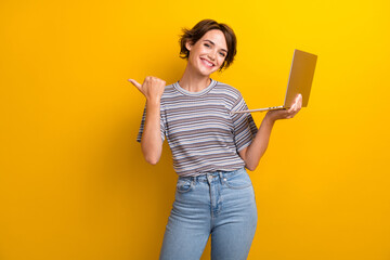 Poster - Portrait of satisfied girl with short hairdo wear grey t-shirt hold laptop directing empty space isolated on yellow color background