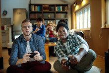 Friends playing video games together, group of young people with game controllers, multiethnic gamers on couch, casual gaming session, fun time at home