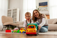Young Mother With Her Little Son Playing At Home With Toys On The Floor, 2 Year Old Boy Holding Toy Car And Having Fun