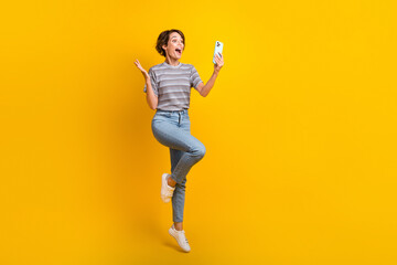 Poster - Full body portrait of impressed carefree lady jump use smart phone empty space ad isolated on yellow color background