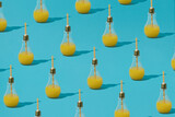 Creative pattern made of light bulb glass with orange juice and straw against pastel blue background. Minimal summer refreshment concept. Beach drink idea.