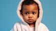 An infant in sadness, wearing a tiny bathrobe, set against a soft blue studio background.