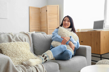 Sticker - Young Asian woman with pillow sitting on sofa at home