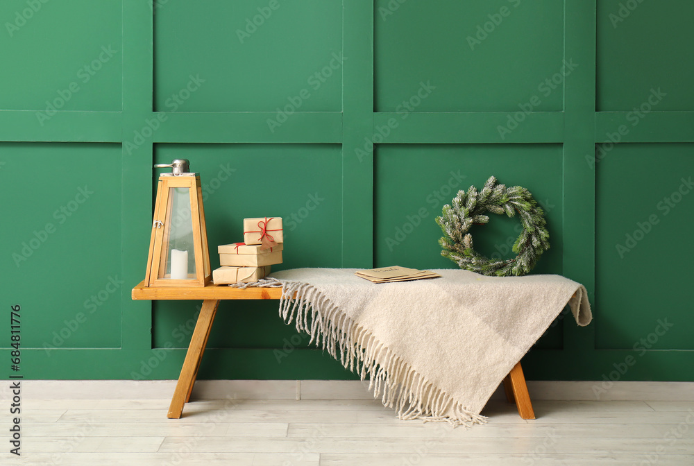 Bench with Christmas wreath, gift boxes and blanket near green wall