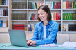 © Valerii Honcharuk - Young female university student studying inside library, typing on laptop computer