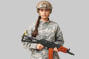 Wall Mural - Confident female soldier in uniform with Ukrainian flag patch on sleeve and assault rifle against grey background