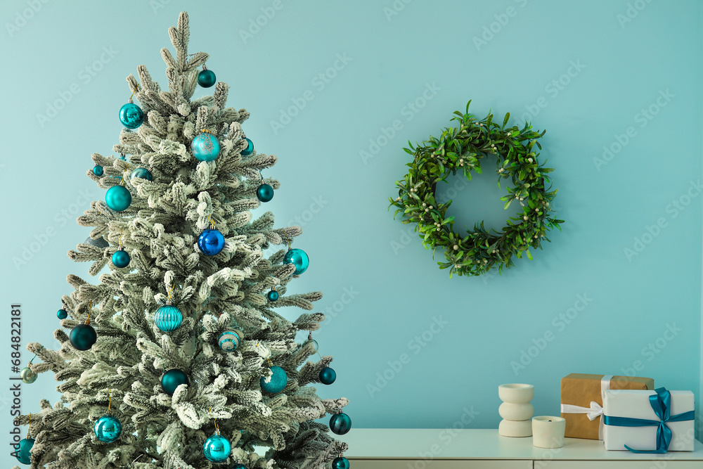 Beautiful Christmas tree with shelving unit near blue wall