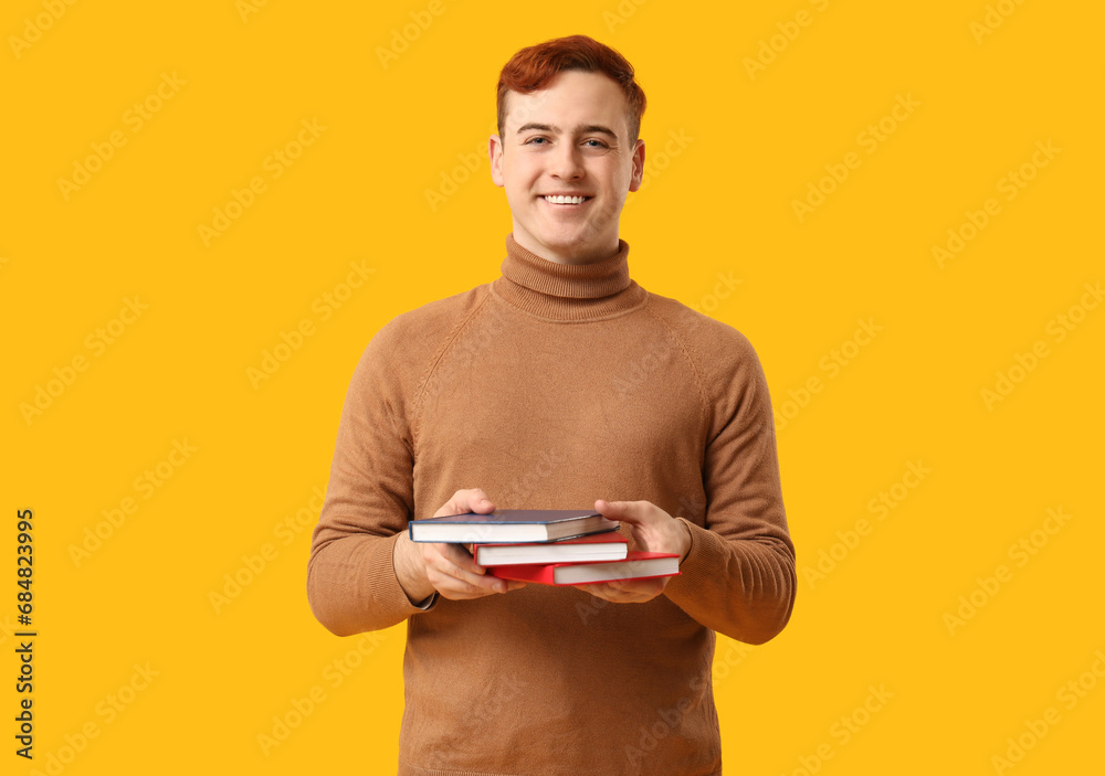 Young man holding books on yellow background