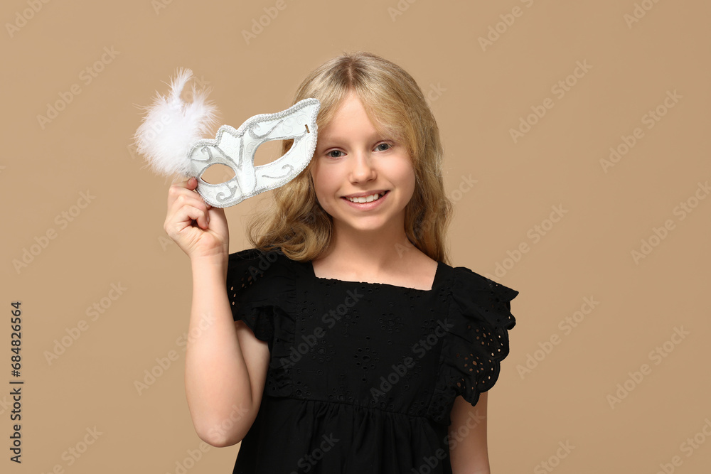 Little girl with carnival mask on beige background