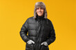 © Pixel-Shot - Young man in black stylish puffer jacket and hat on yellow background