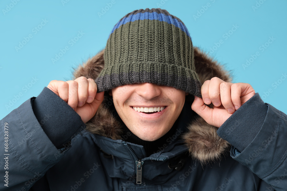 Young man in stylish puffer jacket and hat on blue background