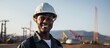 In the vast space of a construction site, a young black man, donning a safety hat, dons a happy face while his portrait captures his dedication as an engineer in the oil industry, tirelessly working