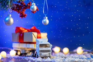 Wall Mural - Toy truck carrying Christmas gifts, blue background, snow and garlands, copy space