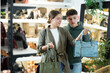 Young man with girl friend inspects shop window and is looking for modern, fashionable and roomy shoulder bag. In leather goods store, customers make choice of product with reasonable price