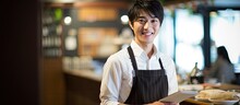 In A Quaint Japanese Cafe, A Young Man With A Charming Smile Works As A Model Employee, Serving Espresso To Customers While His Team Collaborates On Tasks And Updates A Blackboard With The Day's